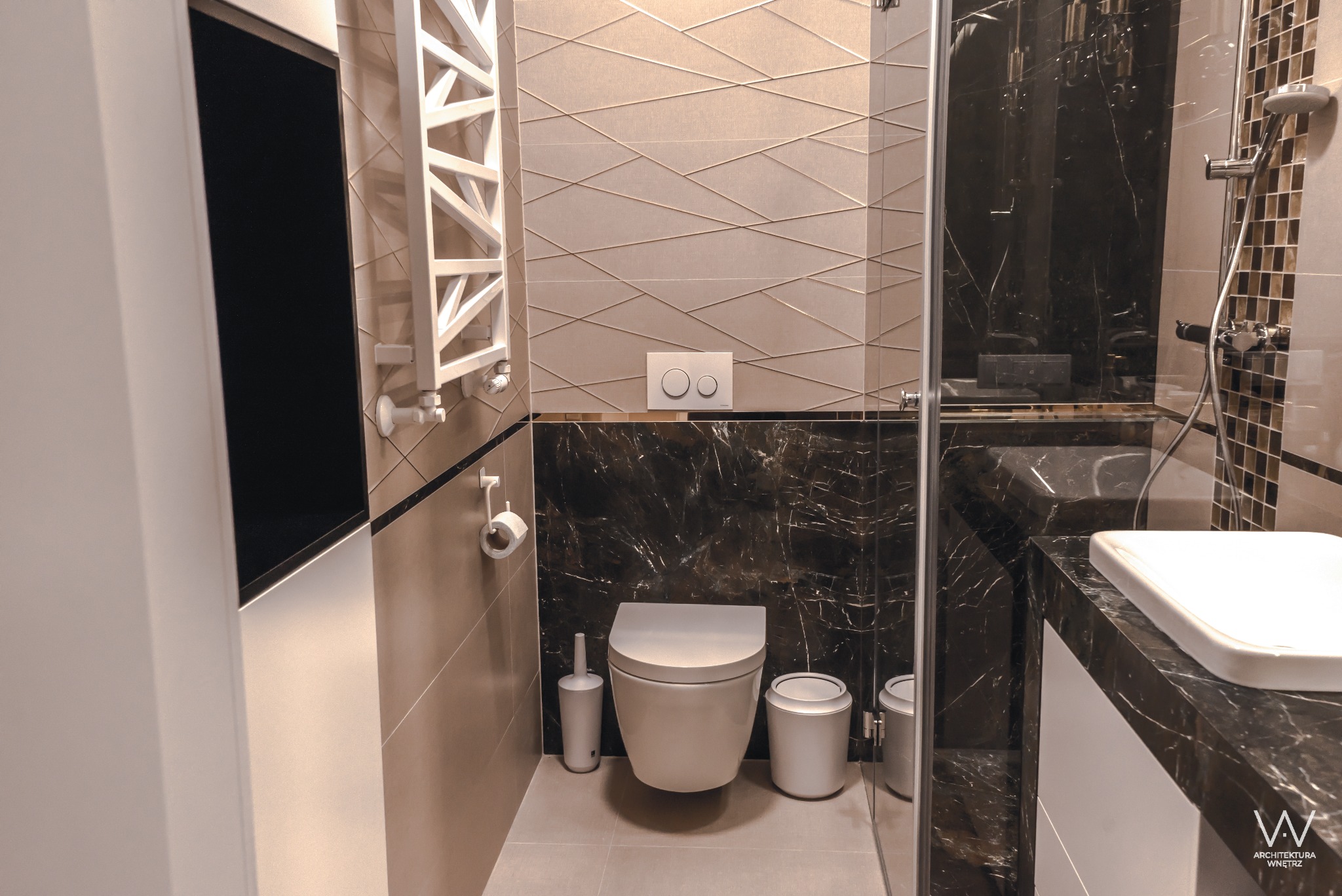 Nowoczesna łazienka z beżowo-czarnymi płytkami, podwieszana toaleta z dwoma przyciskami, grzejnik drabinkowy i kabina prysznicowa ze szklanymi drzwiami.