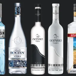 Kolekcja siedmiu różnych butelek wódki o różnych markach i wzorach etykiet, ustawionych na ciemnym tle, prezentujących różnorodność oferty.