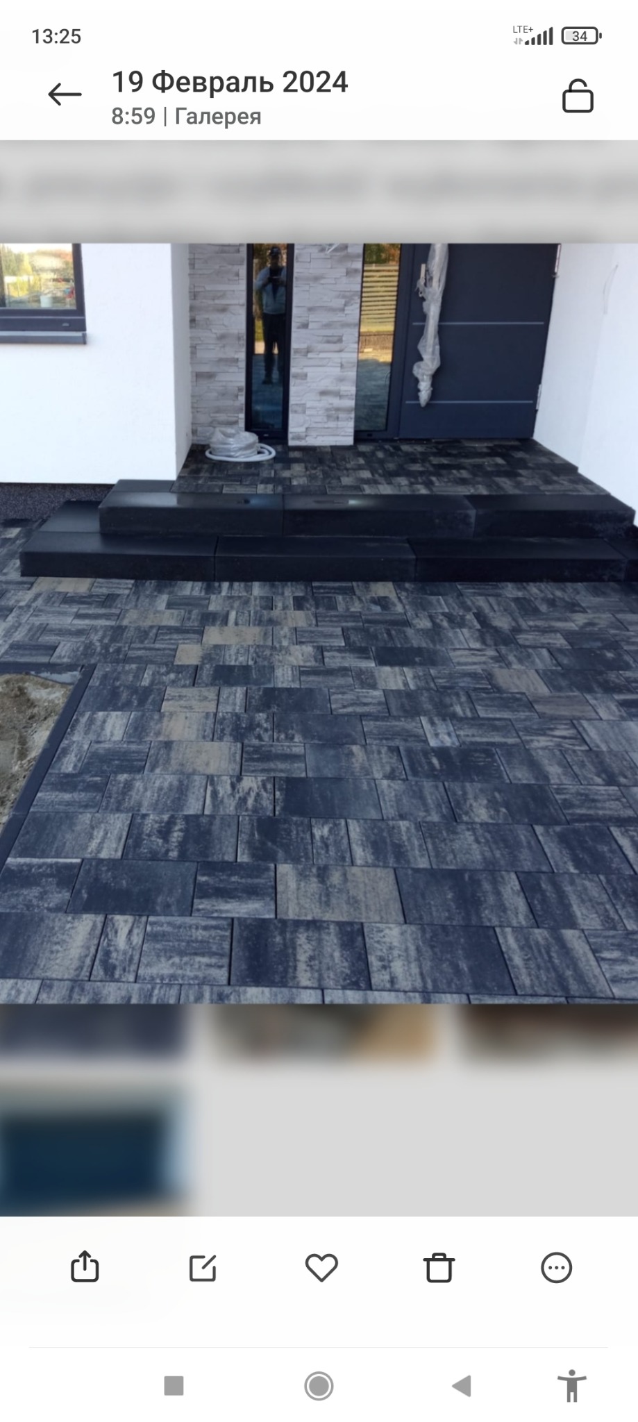 Nowoczesne wejście do domu wyłożone szarą kostką brukową o nieregularnym wzorze, widoczne trzy stopnie z ciemnej kostki prowadzące do drzwi wejściowych.