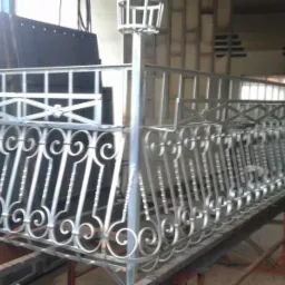 Metalowa konstrukcja balustrady z dekoracyjnymi elementami w kształcie spirali, w trakcie produkcji w warsztacie.