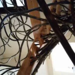 Wewnętrzne schody z drewnianymi stopniami i metalową balustradą stylizowaną na gałęzie drzew, widok z dołu na okno dachowe.