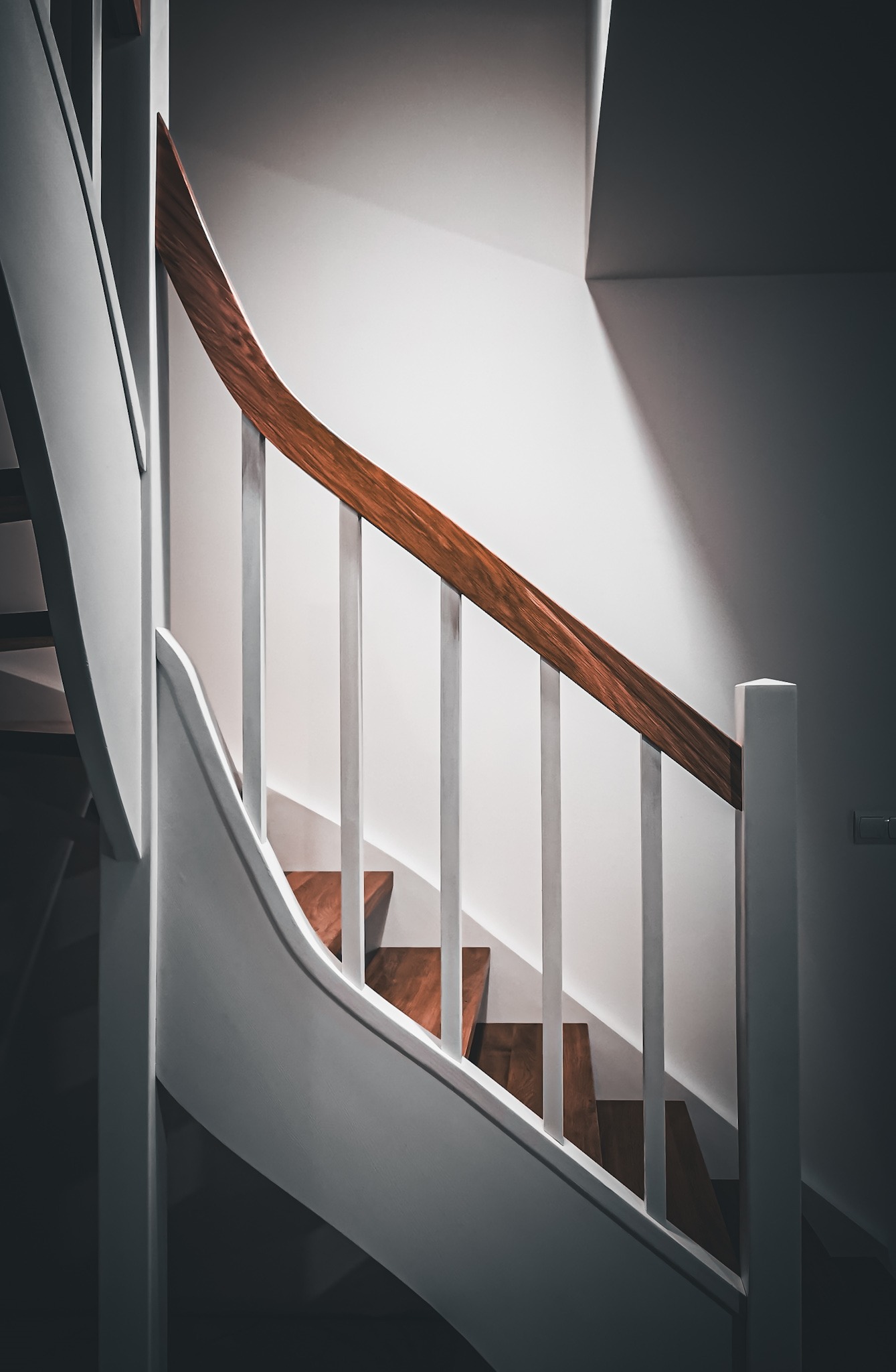 Białe schody z drewnianymi stopniami i poręczą z ciemnego drewna, widok z dołu, minimalistyczny design.