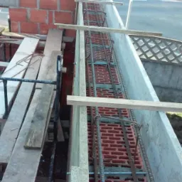 Budowa muru oporowego z cegły zbrojonego stalą, widoczne szalunki i podpory drewniane.