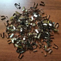 Stos metalowych, chromowanych uchwytów w kształcie litery U na drewnianej powierzchni, rzucających refleksy świetlne.