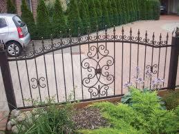 Metalowe ogrodzenie z ozdobnymi elementami w kształcie rozet i kwiatów, na tle podjazdu i zieleni.