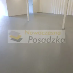 Szara, gładka posadzka żywiczna w jasnym, nowym pomieszczeniu biurowym z widocznymi białymi słupami i ścianami.