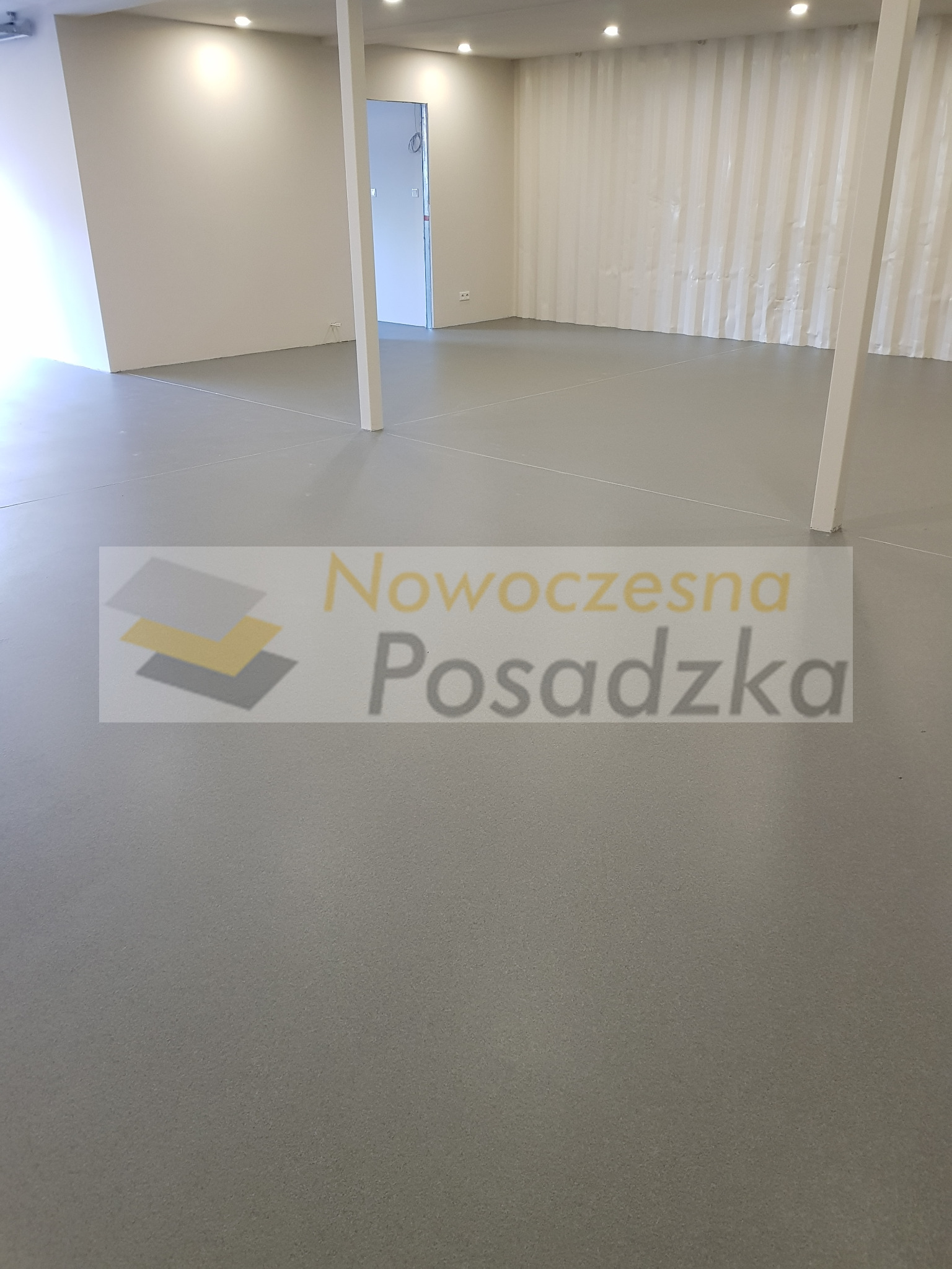Szara, gładka posadzka żywiczna w jasnym, nowym pomieszczeniu biurowym z widocznymi białymi słupami i ścianami.
