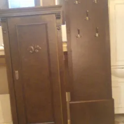 Drewniana szafka z pojedynczymi drzwiami z dekoracyjnym motywem kwiatowym i panel z wieszakami w stylu retro, wykonane w Toruniu, na tle podłogi w szachownicę.