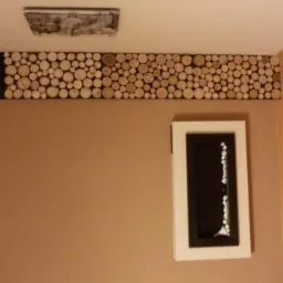 Dekoracyjny pas z drewnianych krążków na ścianie w pokoju, z ramką na ścianie i drewnianą podłogą.