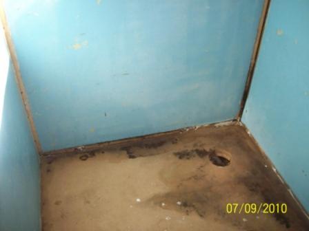 Narożnik zaniedbanej, turkusowej kabiny prysznicowej z widocznymi śladami pleśni i otworem odpływowym w brudnej posadzce.