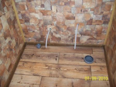 Przygotowane przyłącza wodne i kanalizacyjne w pomieszczeniu z imitacją kamienia na ścianach i panelami podłogowymi.