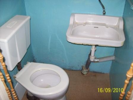Mała łazienka z niebieskimi ścianami, białą umywalką i toaletą. Widoczne rury pod umywalką i data 16/09/2010 w prawym dolnym rogu.