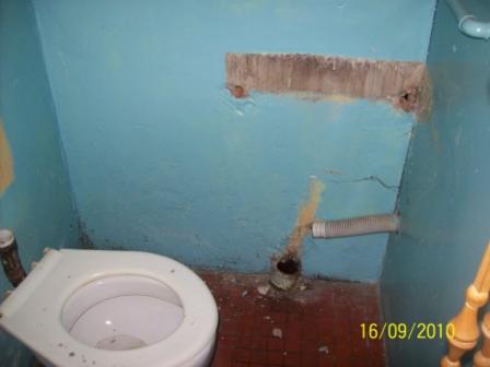 Niefachowo zamontowana toaleta w pomieszczeniu z niebieskimi ścianami, widoczne ślady po starym montażu i wystający wąż odpływowy.