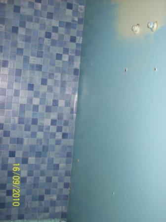 Fragment ściany w łazience z niebieską mozaiką i niebieską, pomalowaną ścianą z widocznymi otworami po mocowaniach.