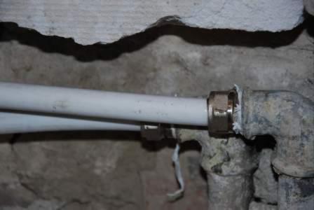 Stare i nowe rury wodociągowe połączone mosiężną złączką, widoczne ślady wilgoci na ścianie i starych rurach.