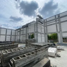 Wnętrze budynku w trakcie budowy z białych bloczków, widoczne szalunki, rusztowania i fragment nieba.