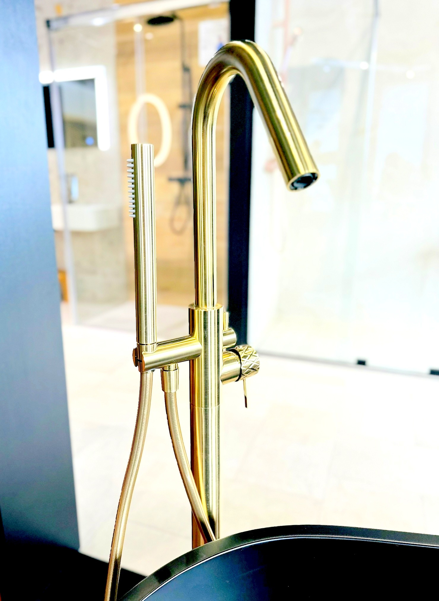 Błyszcząca, złota bateria wannowa wolnostojąca z słuchawką prysznicową na tle jasnej ekspozycji salonu łazienek.