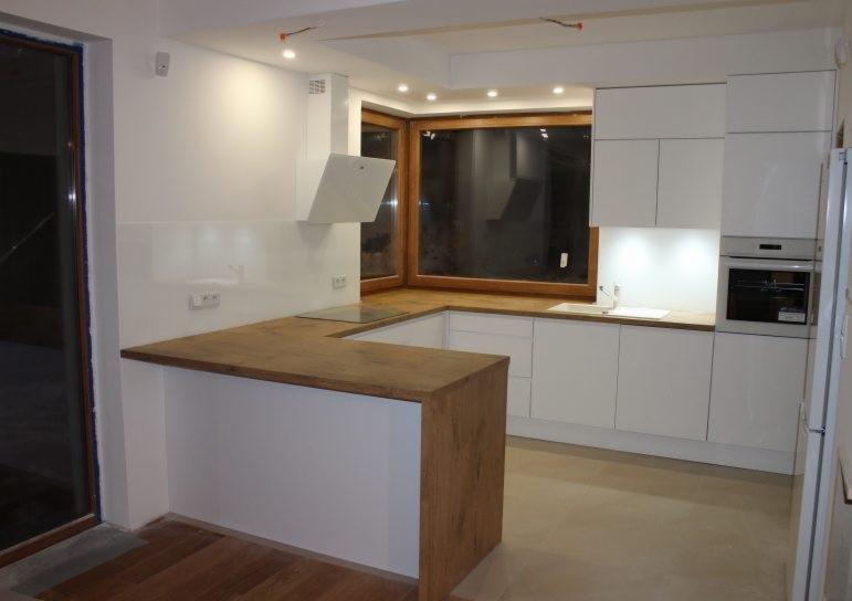 Nowoczesna, jasna kuchnia z białymi szafkami i blatem z drewna dębowego, oświetlenie punktowe, okno z drewnianą ramą, minimalistyczny okap