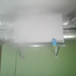 Zamontowana centrala rekuperacyjna z widocznymi przewodami wentylacyjnymi w pomieszczeniu w Wieluniu. Biała obudowa urządzenia na zielonej ścianie.