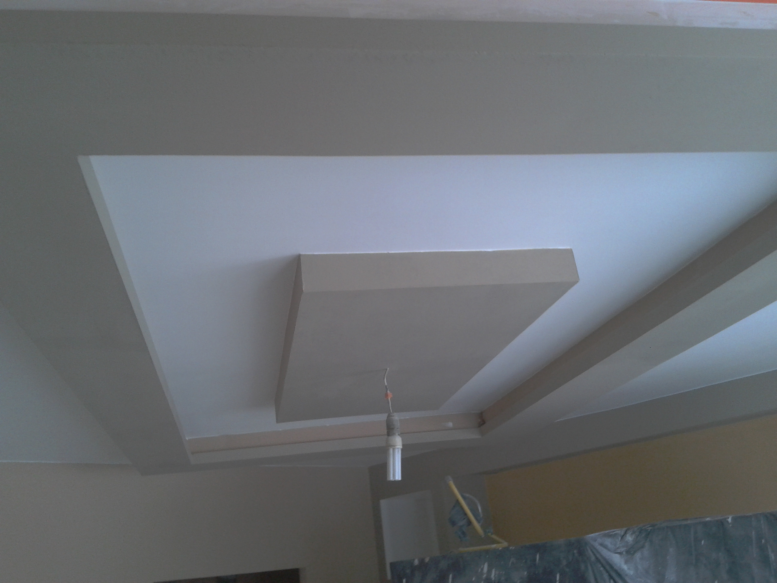 Wykończony sufit podwieszany w pokoju, z widoczną lampą i elementami dekoracyjnymi. Nowoczesny design z geometrycznymi kształtami i świeżym malowaniem.