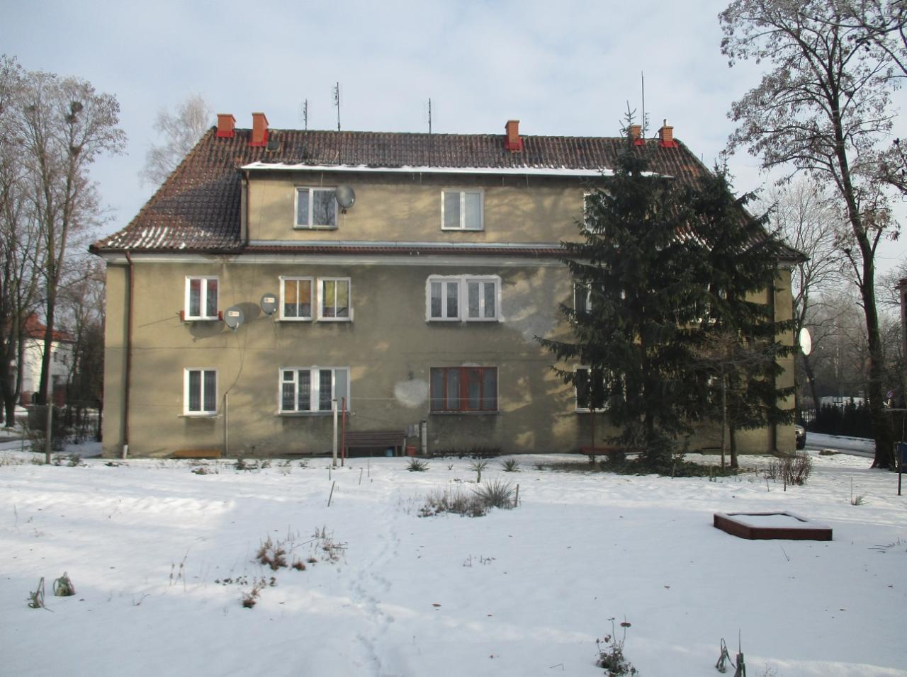 Trzypiętrowy budynek mieszkalny z brązowym dachem i beżową elewacją w zimowej scenerii, Ciechanów II.