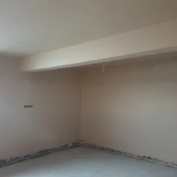 Świeżo otynkowane wnętrze pokoju z widocznymi kablami elektrycznymi wystającymi ze ściany i z sufitu, przygotowane do dalszych prac wykończeniowych.