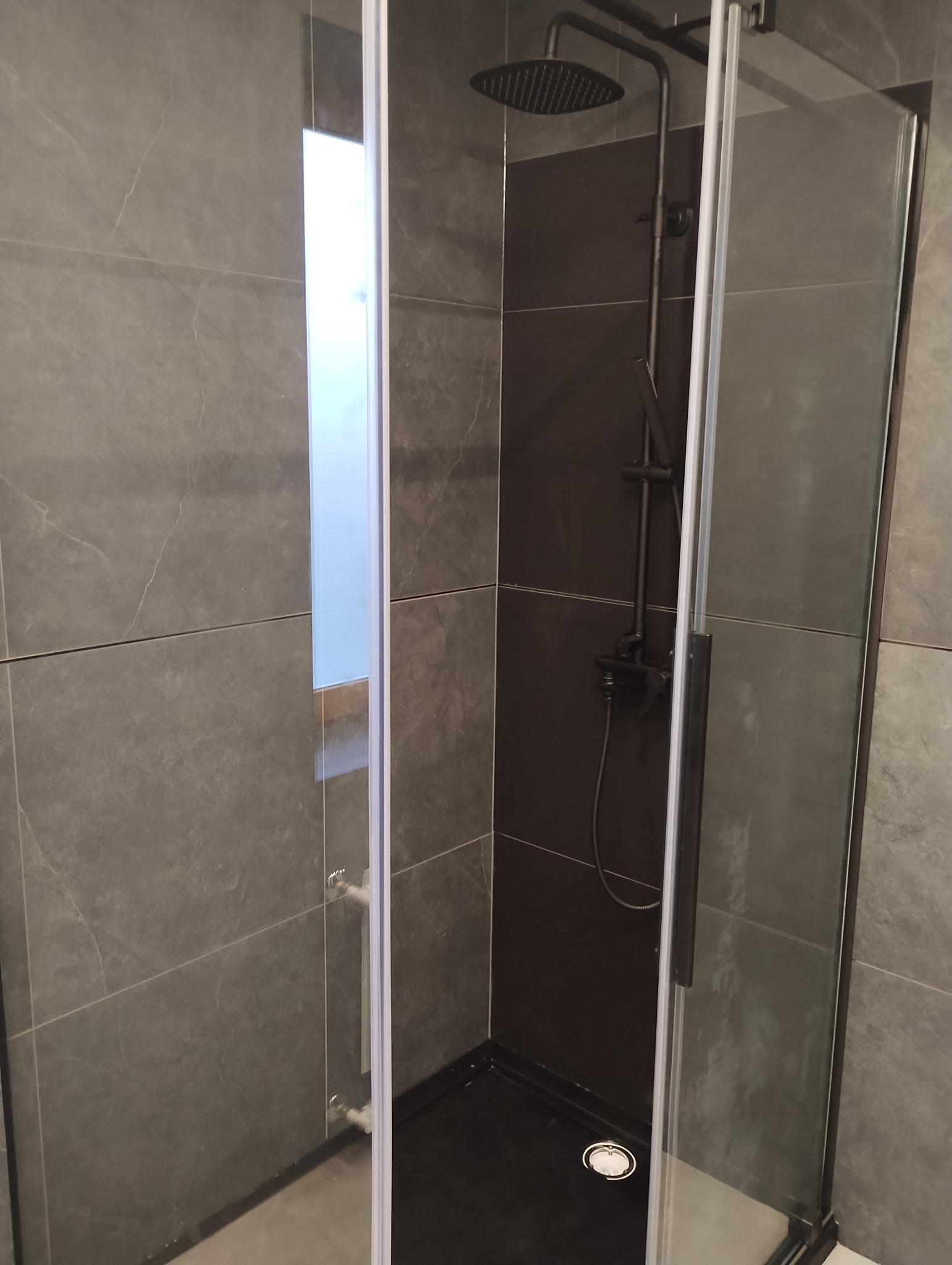 Nowoczesna kabina prysznicowa z czarną armaturą i szarymi płytkami w łazience w Kamieniu Pomorskim.