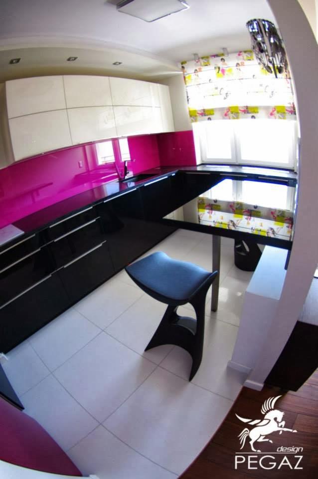 Nowoczesna kuchnia z białymi szafkami, czarnym blatem i różowym panelem szklanym, z krzesłem barowym i roletą okienną w kwiaty, widziana z szerokiego kąta.