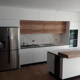 Nowoczesna kuchnia z białymi szafkami, drewnianymi akcentami nad blatem i wyspą, stalową lodówką side-by-side i minimalistycznym oświetleniem.