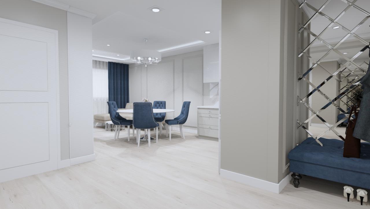 Jasne wnętrze mieszkania z okrągłym stołem i krzesłami w odcieniach niebieskiego, widoczne lustro z geometrycznym wzorem i pufa w przedpokoju.