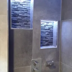 Nowoczesna łazienka z wnękami oświetlonymi LED z mozaiką w odcieniach szarości i czerni, bateria umywalkowa w minimalistycznym stylu.