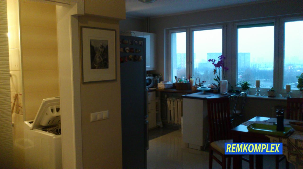 Ukończone wnętrze mieszkania: widok na kuchnię z oknem, pralkę w łazience i obraz na ścianie. Całość utrzymana w jasnych, stonowanych barwach.