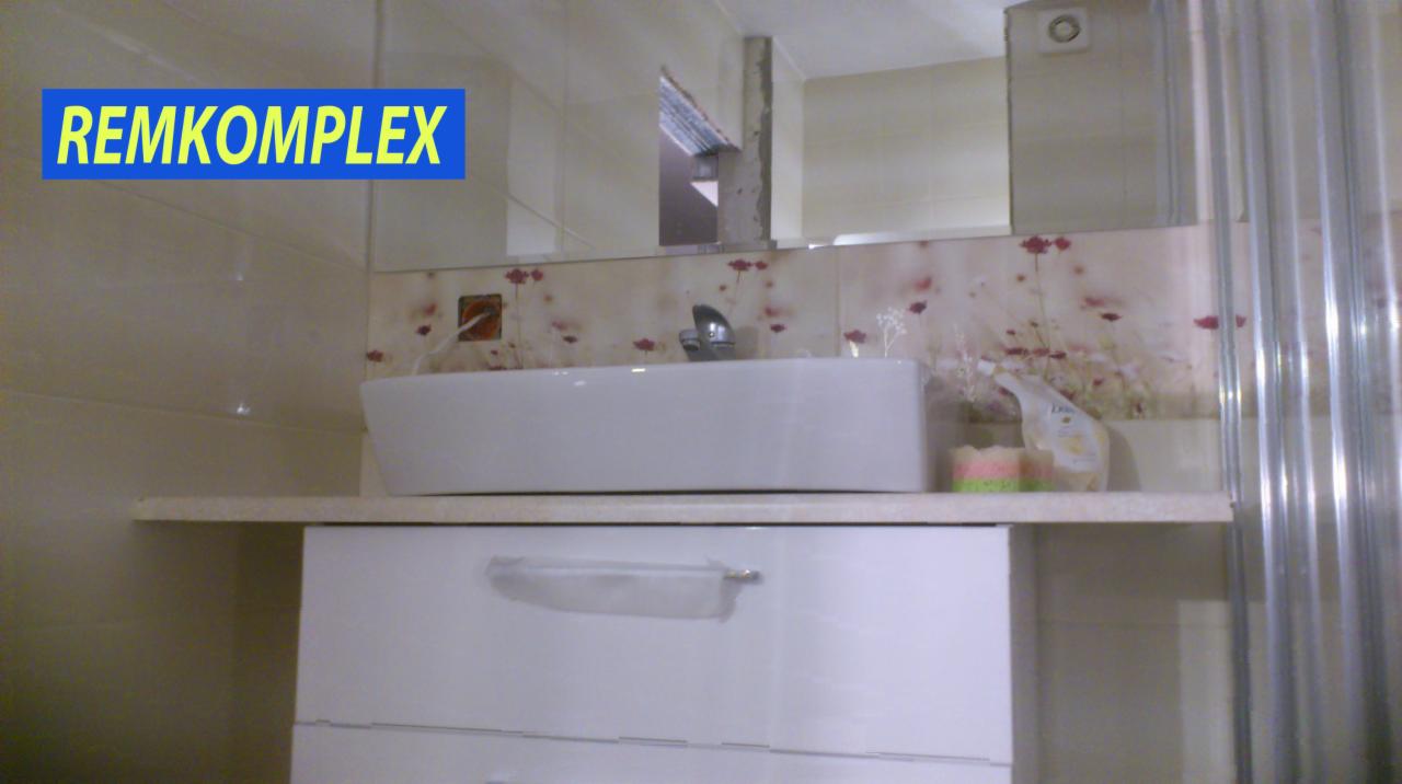 Umywalka nablatowa w białej szafce łazienkowej, z baterią i dekoracyjną mozaiką nad blatem, widok z boku z zasłoniętą kabiną prysznicową.