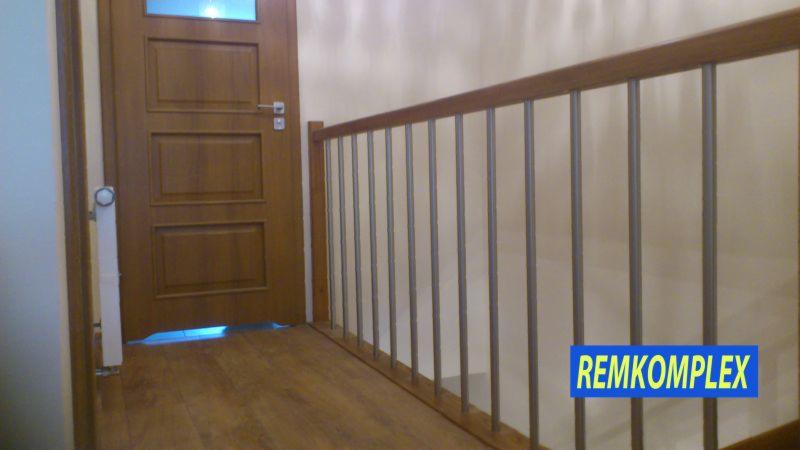 Wnętrze: drewniane schody z metalowymi barierkami i drzwiami. Parkiet na podłodze. Widoczny fragment ściany. Ujęcie z dołu, perspektywa schodów.