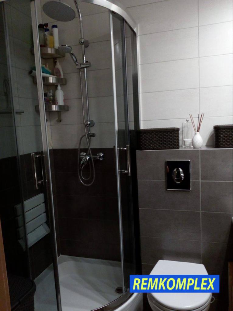 Wykończona łazienka z kabiną prysznicową z hydromasażem, półkami na kosmetyki i siedziskiem, obok toaleta i szare płytki z dekoracyjnymi koszykami i dyfuzorem zapachowym.