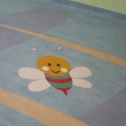 Kolorowa podłoga z wzorem pszczoły na tle geometrycznych kształtów w odcieniach szarości, błękitu i żółci.