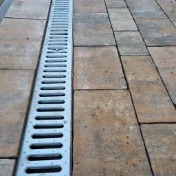 Nowo ułożona kostka brukowa w odcieniach brązu i szarości z zamontowanym, metalowym odpływem liniowym.