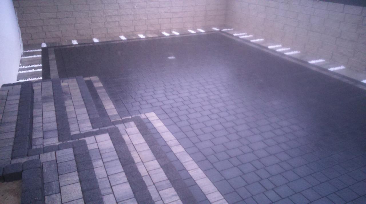 Ułożona, ciemnoszara kostka brukowa na powierzchni z widocznymi jasnymi, liniowymi elementami dekoracyjnymi wzdłuż krawędzi i schodów.