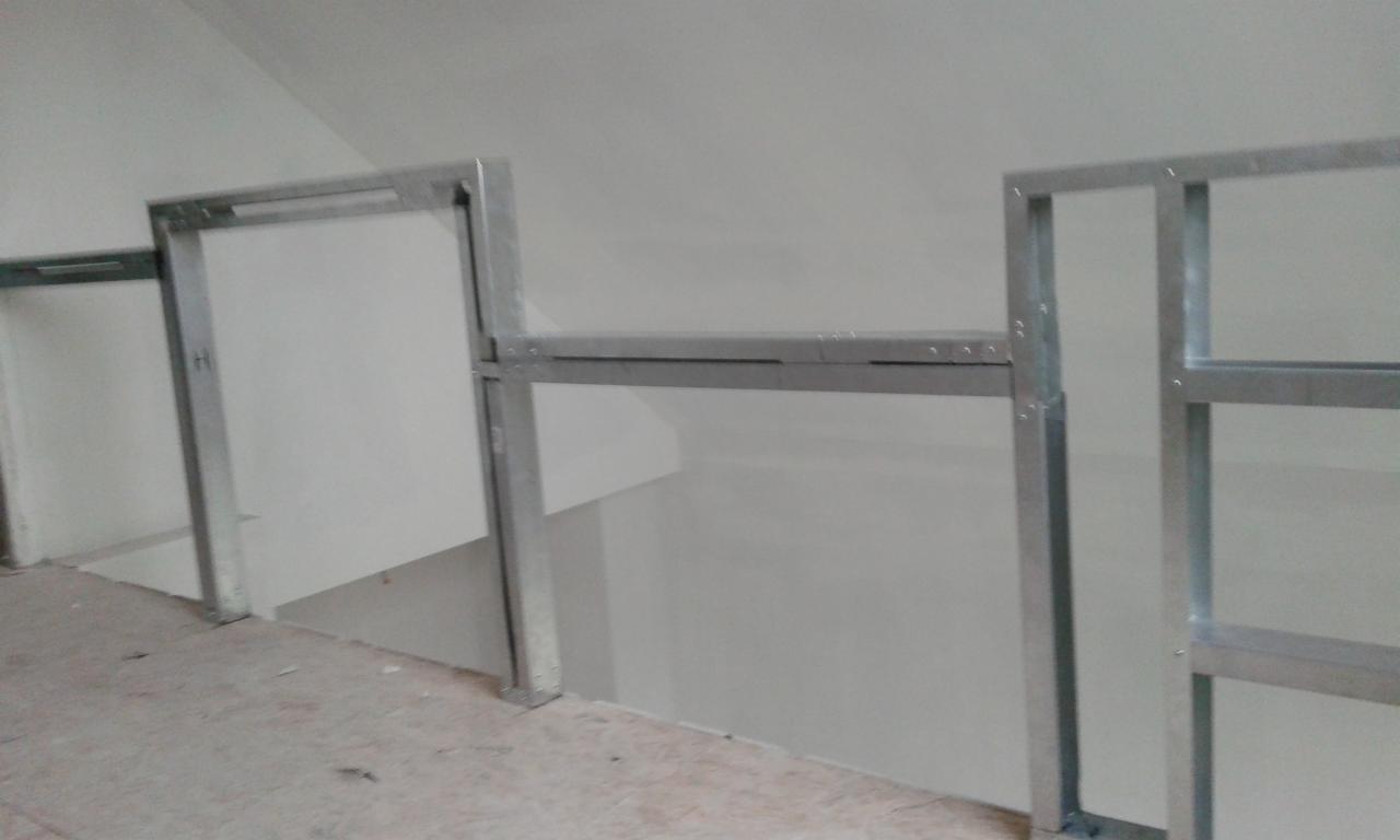 Konstrukcja z metalowych profili, prawdopodobnie pod ściankę działową, widoczna na tle białej ściany w trakcie prac budowlanych.