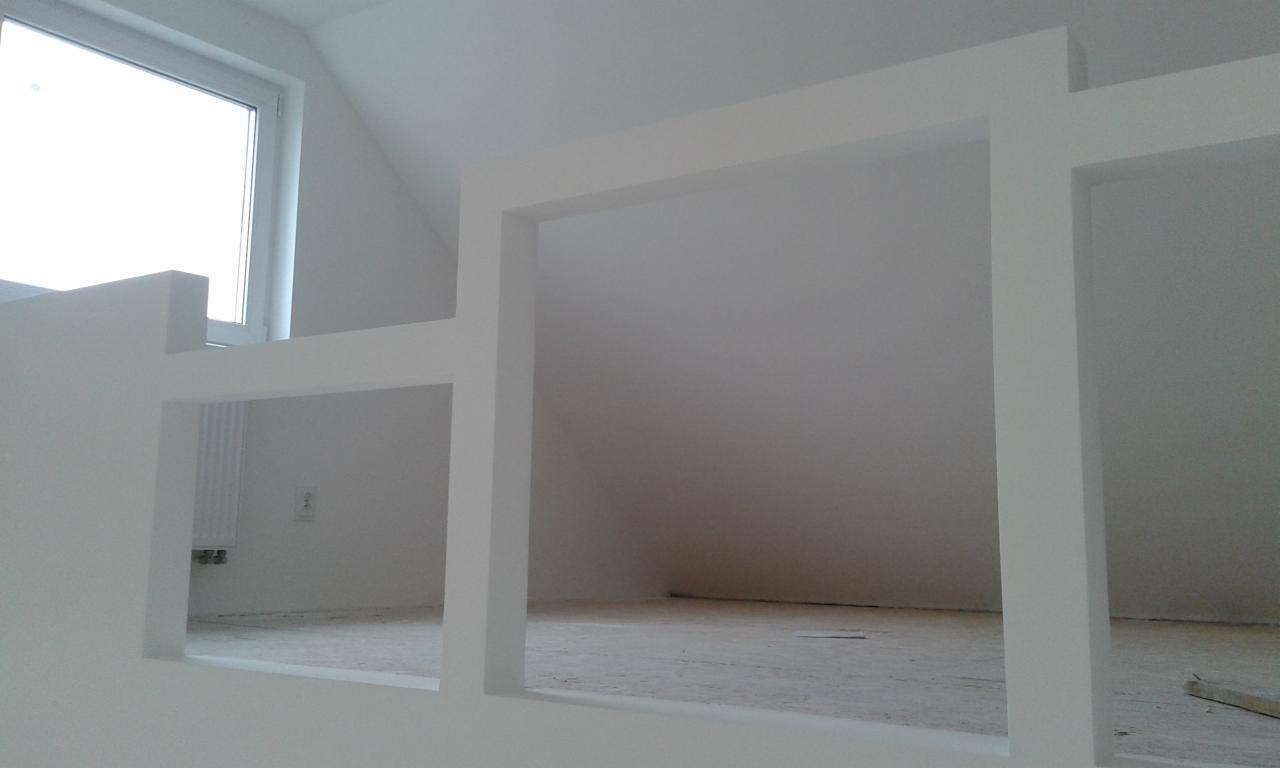 Wnętrze poddasza w trakcie wykańczania, z widoczną konstrukcją ścianek działowych z płyt gipsowo-kartonowych i oknem dachowym.