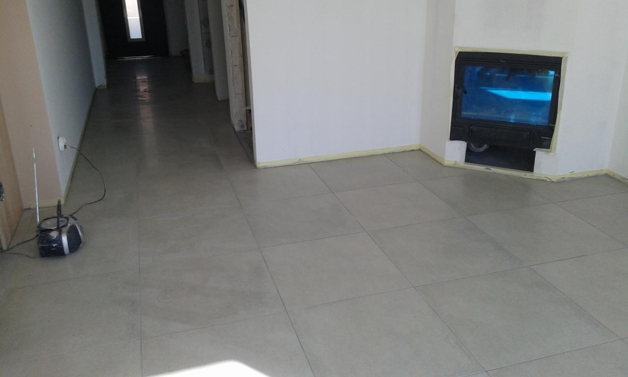 Ułożone szare płytki podłogowe w nowym wnętrzu z kominkiem zabezpieczonym taśmą malarską, Polanów. Na podłodze stoi radio.