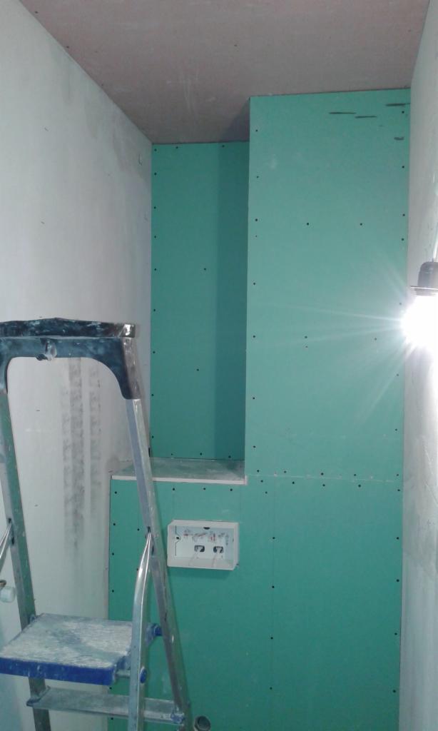 Ściana z płyt kartonowo-gipsowych w trakcie zabudowy, widoczna puszka elektryczna i drabina malarska, sufit częściowo wykończony.