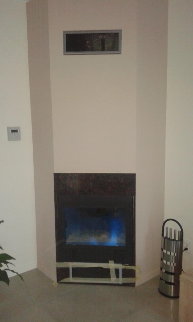 Wnęka kominkowa z wkładem, obudowana płytami w kolorze kremowym, zabezpieczona taśmą malarską na etapie wykończenia.