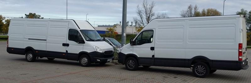 Dwa białe busy dostawcze Iveco zaparkowane na parkingu, widoczne z boku i przodu, z szarym samochodem osobowym między nimi.