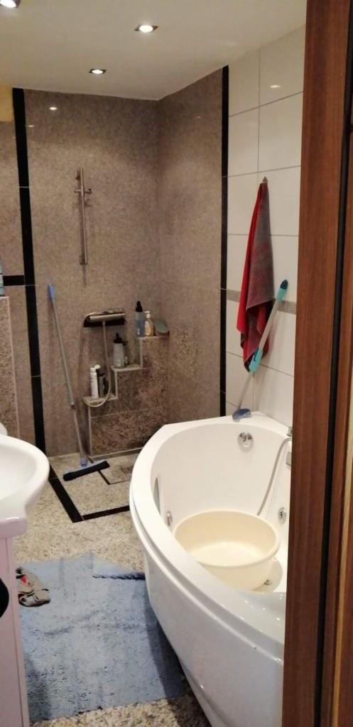 Niedokończona łazienka z narożną wanną jacuzzi, mopem opartym o ścianę prysznica i miską w wannie.