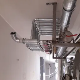 Kompleksowy system rur i zaworów ze stali nierdzewnej zamontowany pod sufitem, z widocznymi licznymi złączkami, zaworami z czerwonymi uchwytami i elementami wsporczymi