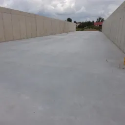 Gładka, szara powierzchnia betonowa pomiędzy betonowymi ścianami, dwa żółte wiadra w rogu, tło niebieskiego nieba z chmurami.