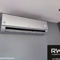 Zamontowany srebrny klimatyzator LG z wyświetlaczem temperatury 23 stopnie Celsjusza na szarej ścianie, widoczny fragment sufitu i logo RWS Klimatyzacja z adresem strony i numerem telefonu w prawym...