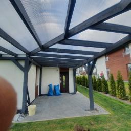 Firma remontowo budowlana Fryc Łukasz - Zadaszenie tarasu z poliwęglanu i ciemnego drewna, widoczne dwa worki budowlane przy drzwiach wejściowych i częściowo przesłonięte ujęcie