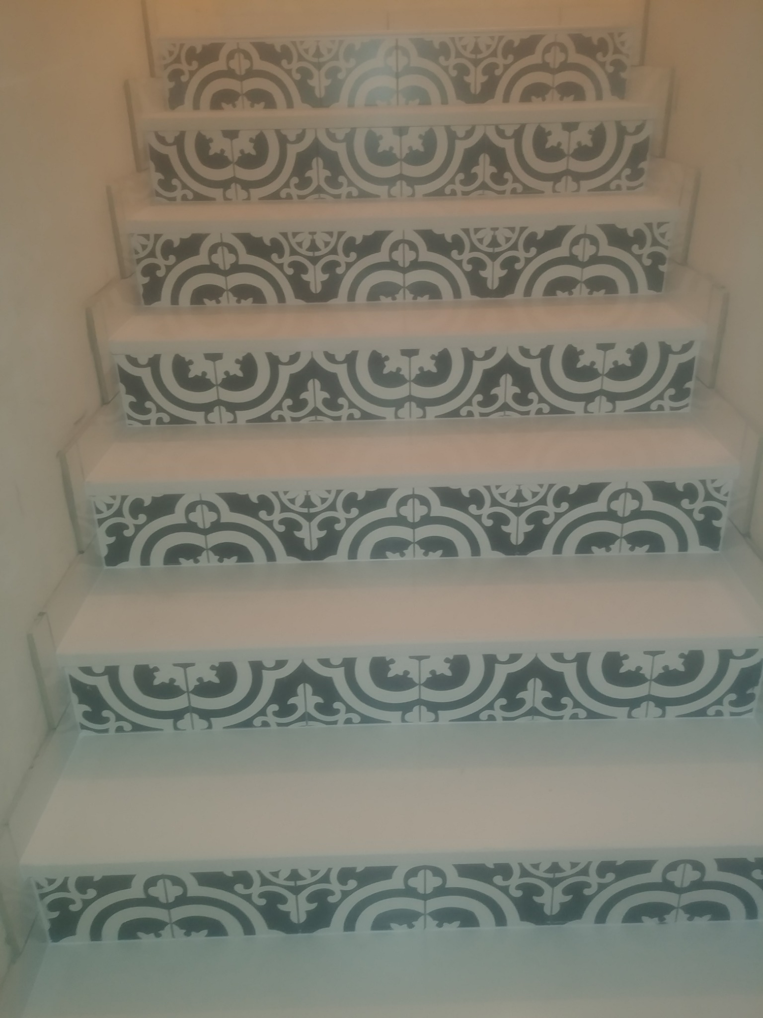 Schody wykończone białymi płytkami z dekoracyjnym, czarno-białym wzorem na krawędziach stopni, widziane z dołu.